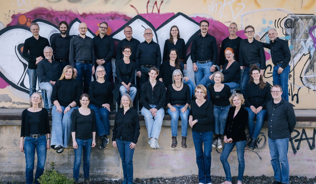 Gemischter Chor vor einer Wand, die mit Graffiti gestaltet ist